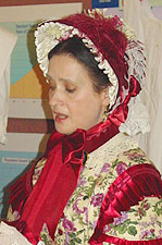 A proper full bonnet with lace and flowers inside the brim and ostrich feathers on the outside, styled as of the 1860s.