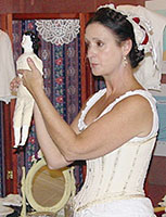Jane demonstrating the desired figure shape as shown on an 1860s period doll while wearing an 1860s style corset.